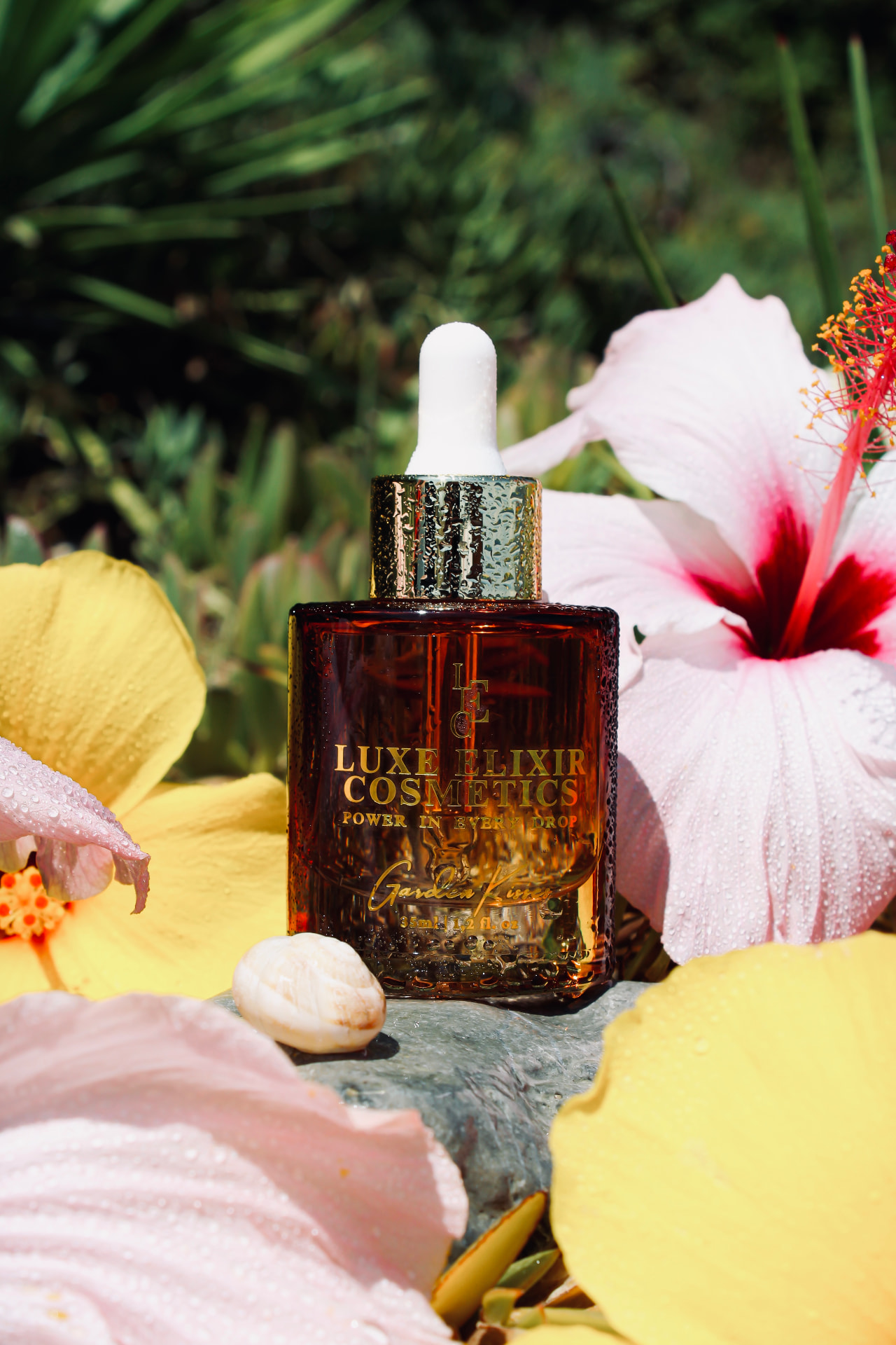 Garden Kisses perfume oil bottle by Luxe Elixir Cosmetics resting among dew-covered hibiscus blooms