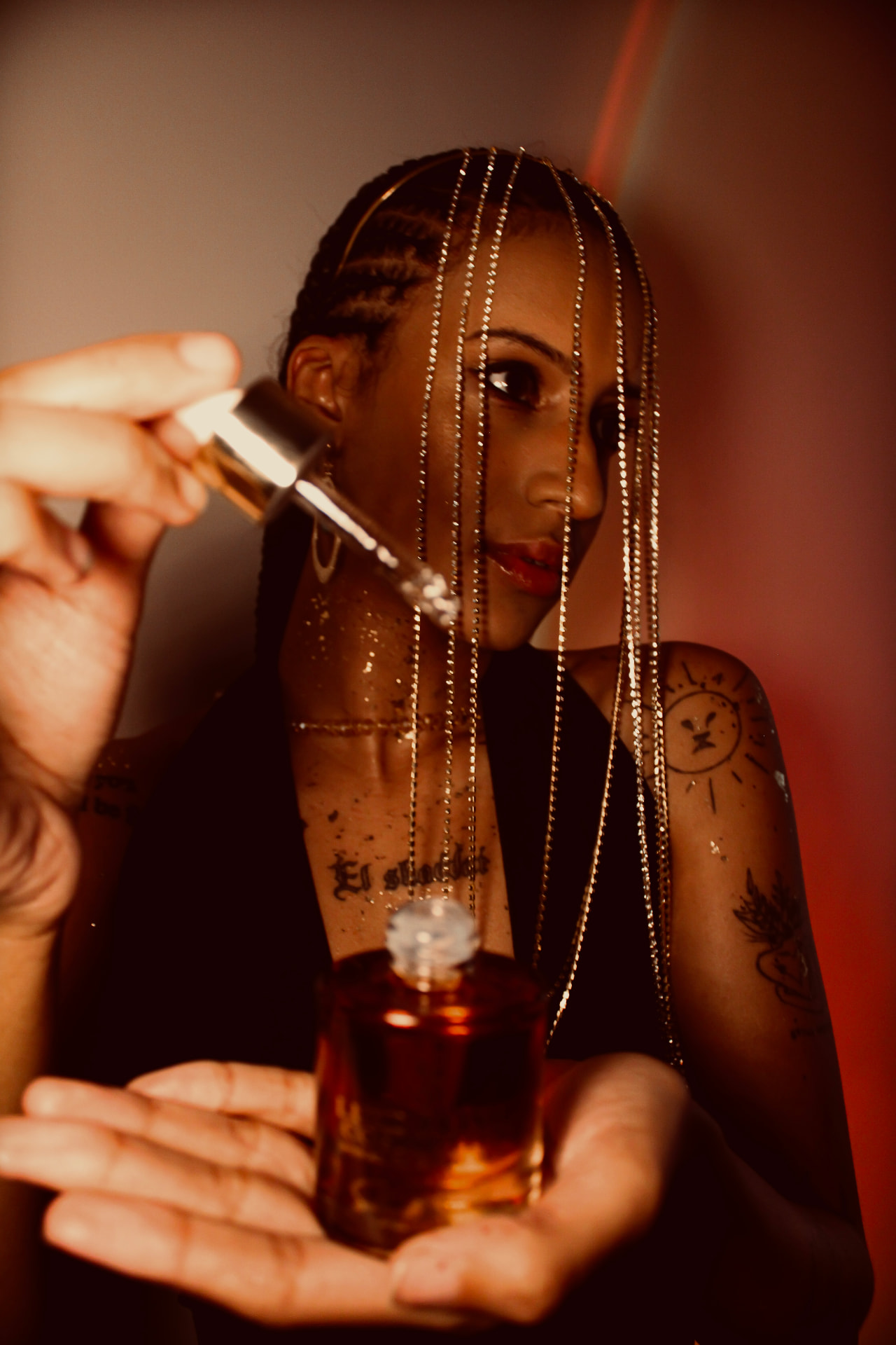 Close-up of a golden dropper being lifted from a Luxe Elixir Cosmetics perfume oil bottle in warm red light